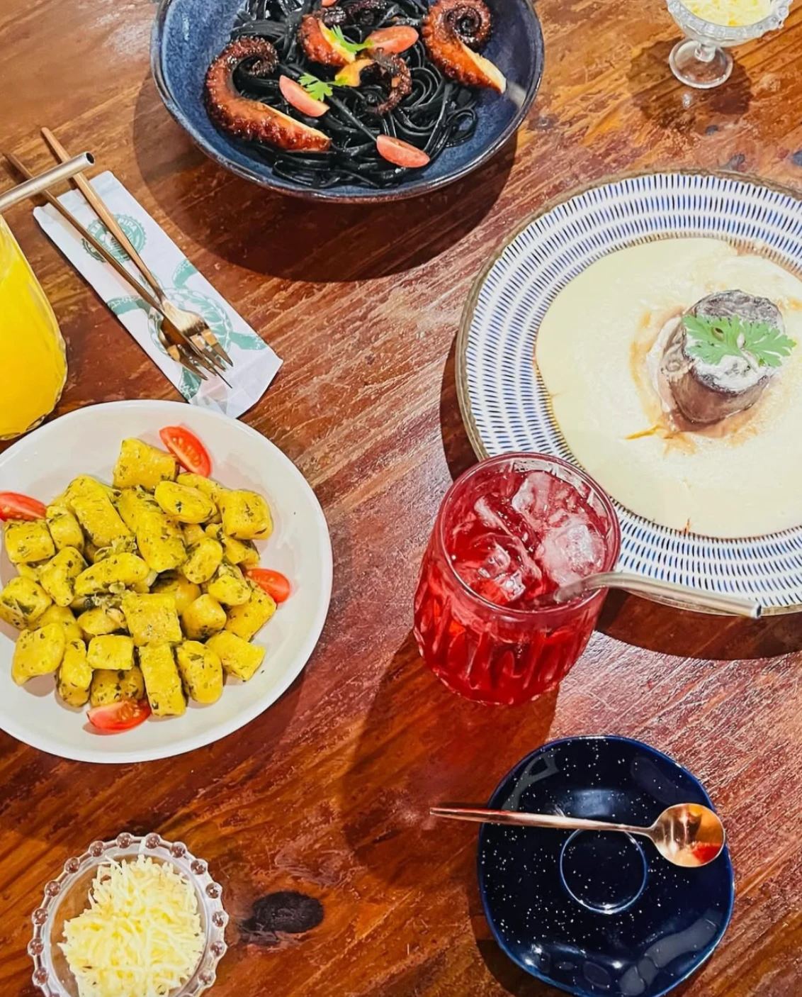 Mesa de almoço com linguine nero com polvo, nhoque ao pesto, mignon com purê e drink vermelho